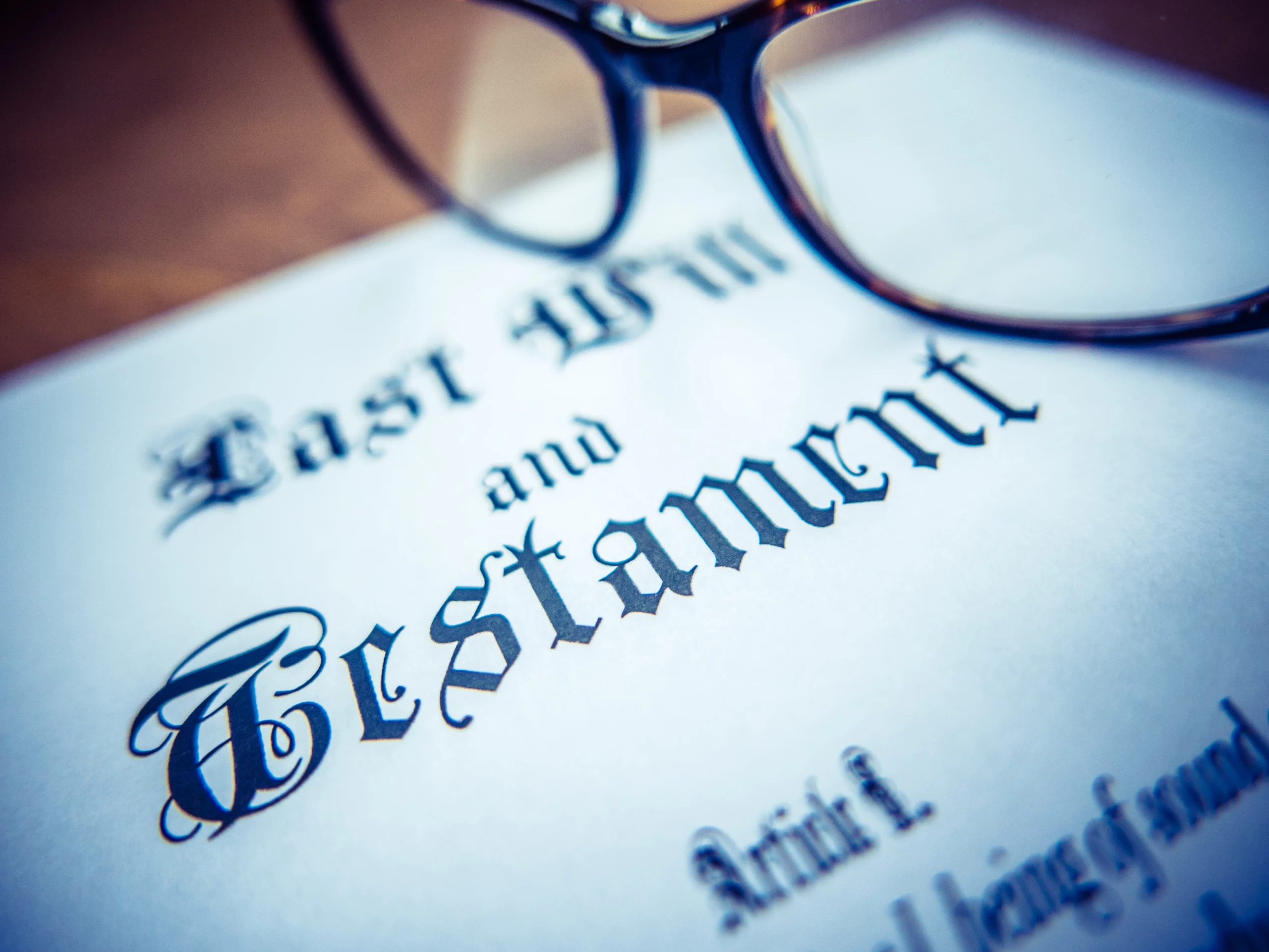 Close-up of a "Last Will and Testament" document with eyeglasses resting on top, symbolizing legal inheritance matters.